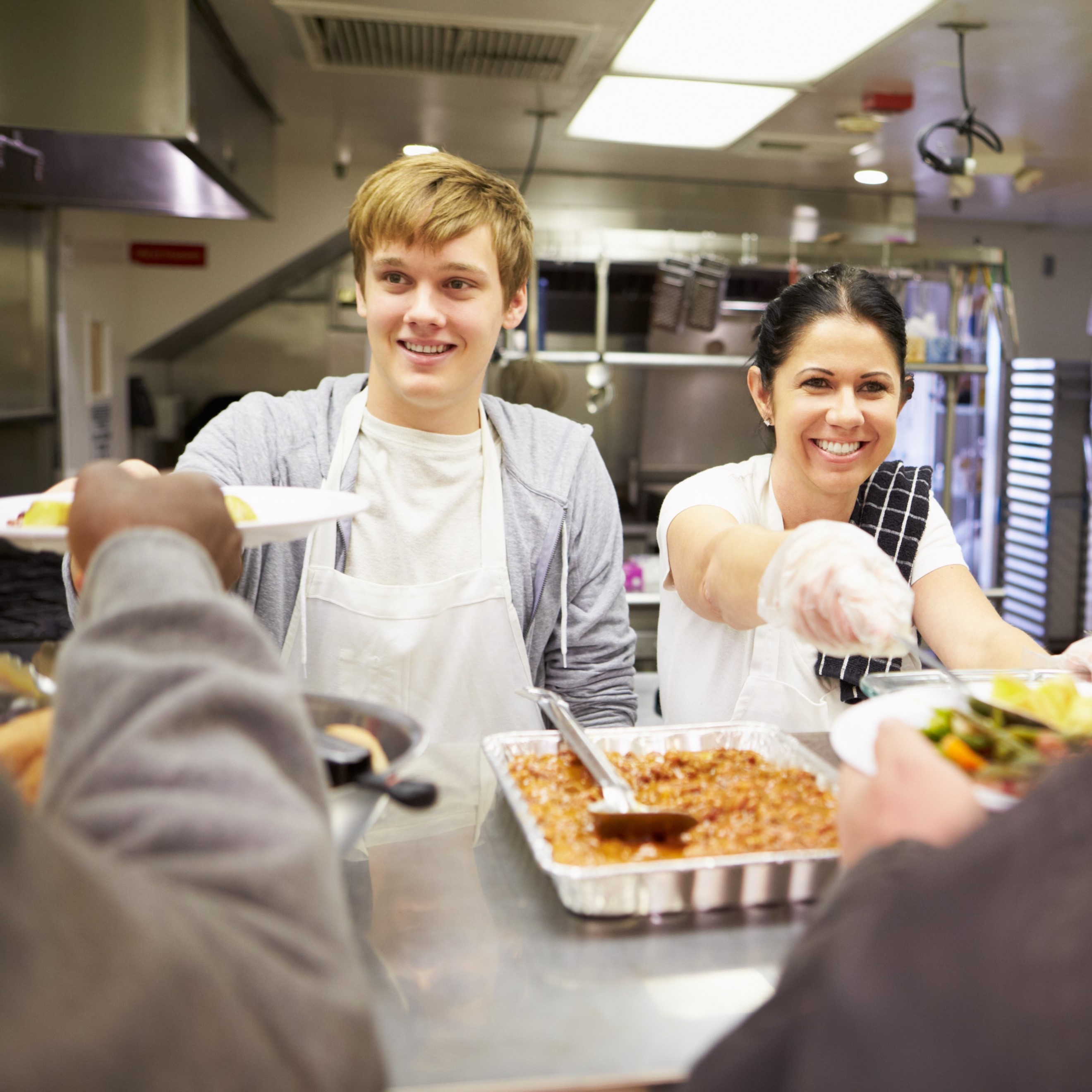 A boy and a woman serve food behind a cafeteria counter